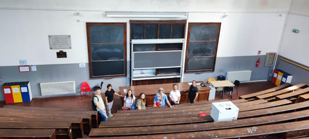 View from the last row of a lecture hall on 6 persons standing with their backs to the blackboard.
